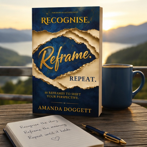 Recognise. Reframe. Repeat. by Amanda Doggett standing on a wooden table beside a blue mug, notebook and pen, with a lake and mountains in the background.